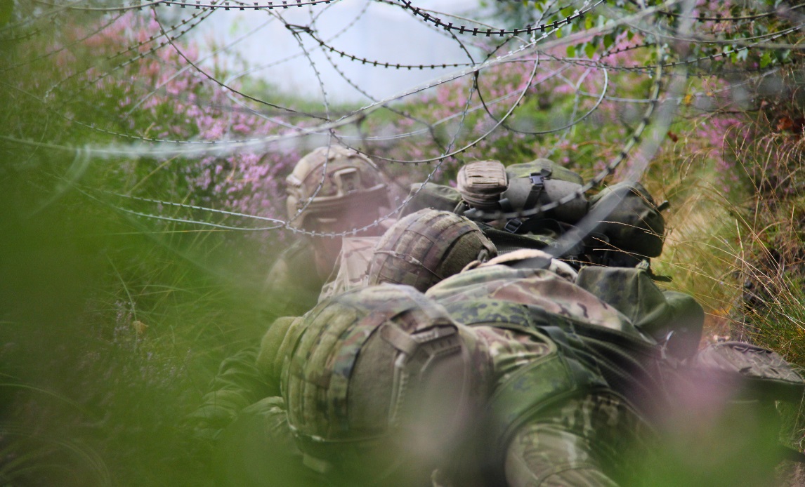 Værnepligtige på feltforhindringsbane i Karup. Her er de på vej under pigtråd med både våben og båre.