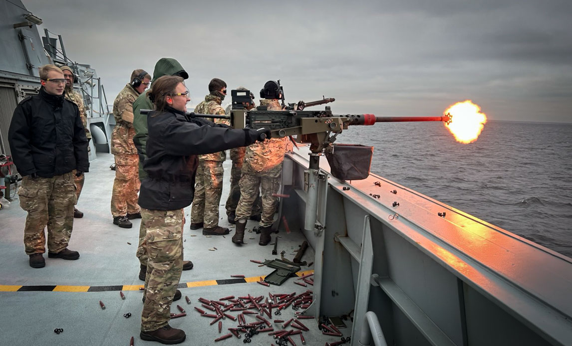 En soldat står på dæk af fregat og skyder med maskingevær