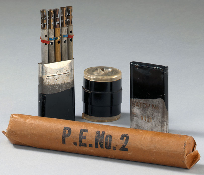 En rulle med PE2 plastisk sprængstof, æske med tidsblyanter og hylster til detonatorer. Farven på tidsblyanterne viser, hvor stor deres tidsforsinkelse er.