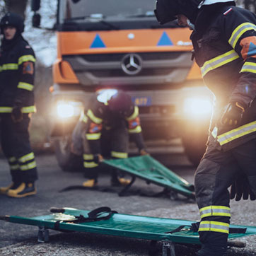 Tre medarbejdere i Beredskabsstyrelsen i uniform blandt grønne båre og orange lastbiler