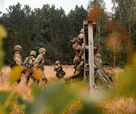 En gruppe værnepligtige på øvelse på vej over en forhindring.